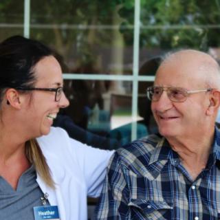A caregiver and an elderly man share a moment of interaction and smiles.
