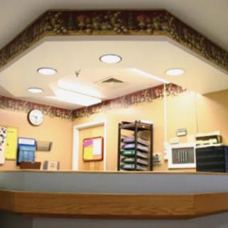 A well-lit reception desk with a clock and stacks of papers on the counter.