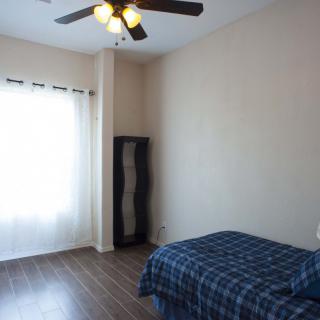 A minimalist bedroom with a single bed, wooden floor, and ceiling fan.