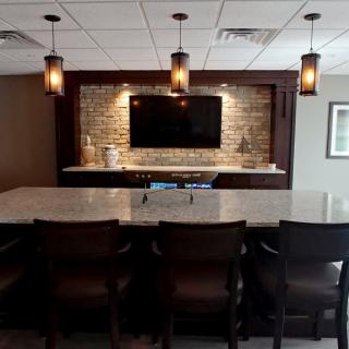 A stylish home bar setup featuring a marble countertop, pendant lights, and a brick accent wall with a mounted TV.