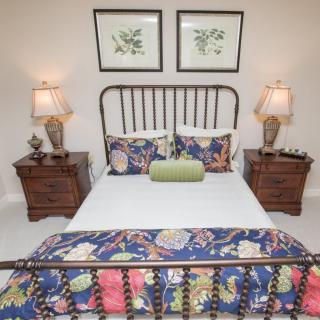 A cozy bedroom with a metal-framed bed, floral bedding, and matching nightstands with lamps.