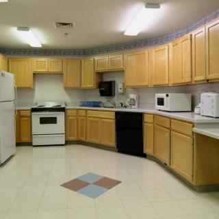 A spacious kitchen featuring light wood cabinets, modern appliances, and tiled flooring.