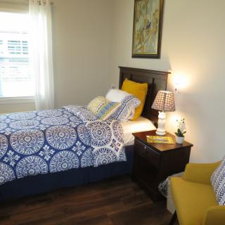 A cozy bedroom with a single bed, bright bedding, and a warm lamp on the nightstand.