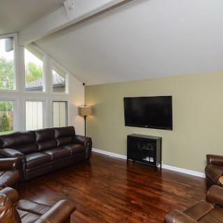 A cozy living room featuring modern brown leather sofas, a flat screen TV, and ample natural light from large windows.