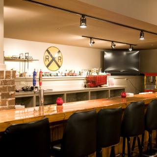A cozy bar with a wooden counter and seating, featuring beverage options and a TV screen.