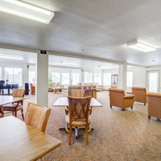 A spacious interior dining area with wooden tables and chairs, well-lit with large windows.