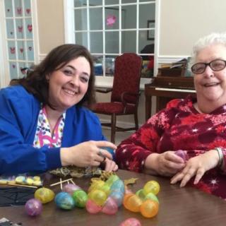 Two women smiling while sitting at a table with colorful eggs.
