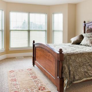 A bright bedroom with a wooden bed, large windows, and decorative carpet.