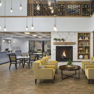 A modern hotel lobby with a cozy seating area featuring yellow chairs and a fireplace.