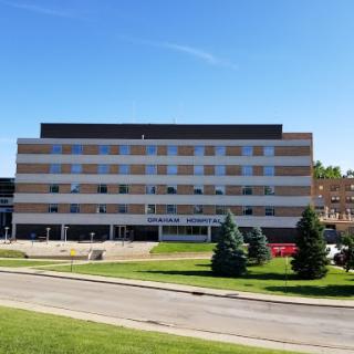 A modern hospital building surrounded by lush green grass under a clear blue sky.