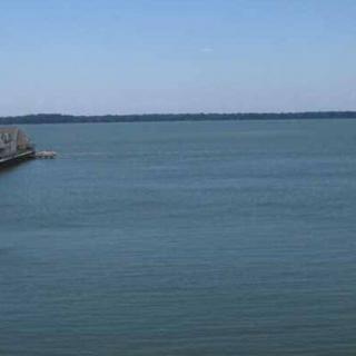 A peaceful view of a lake with a pier extending into the calm water under a clear blue sky.