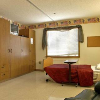 A hospital room with a bed, wooden furniture, and a television.