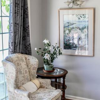 A cozy living room corner featuring a patterned armchair, a small side table with a potted plant, and a framed painting on the wall.