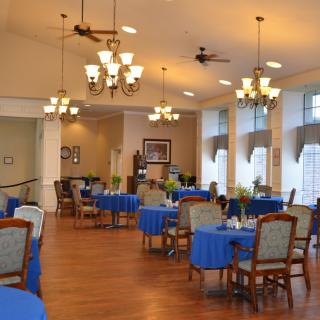 A spacious dining area with tables covered in blue tablecloths and elegant lighting fixtures.