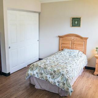 A minimalist bedroom with a single bed, nightstand, and wooden flooring.