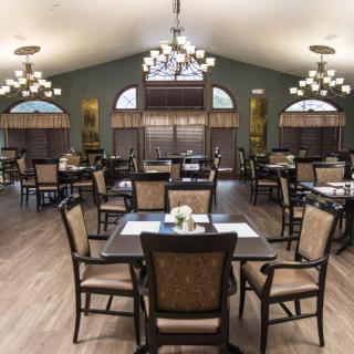A spacious dining room with elegant chandeliers, neatly arranged tables and chairs, and large windows.