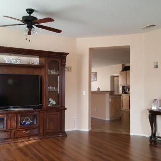 A spacious living room featuring a wooden entertainment center with a television, ceiling fan, and wood flooring.