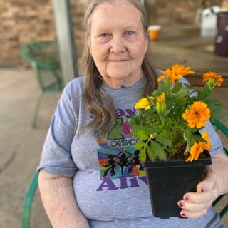 An elderly woman holding a potted flower, enjoying a sunny day outdoors.