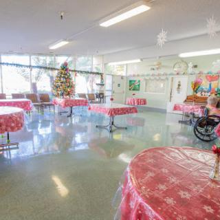 A spacious community center decorated for the holiday season, featuring tables with red covers and a Christmas tree.