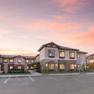 A modern residential building under a colorful sunset sky, with an adjacent parking lot.