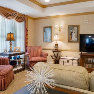 A cozy living room with classic decor, featuring armchairs, a coffee table, and a flat-screen TV.