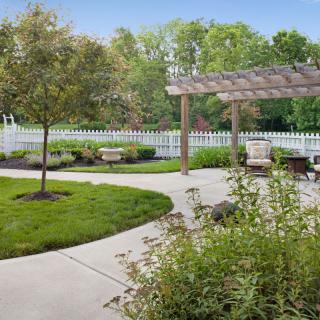 A beautiful garden with a pergola, surrounded by lush greenery and a white picket fence.