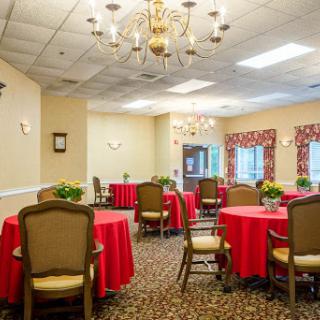 A beautifully arranged dining room featuring round tables with red tablecloths and elegant seating, illuminated by a chandelier.