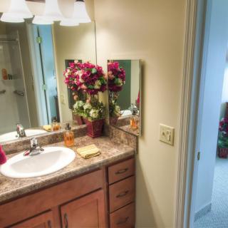 A cozy bathroom with flowers on the countertop and a mirror above the sink.