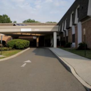 A driveway leading to the entrance of a large building with surrounding greenery.