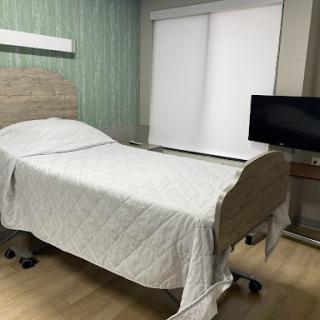 A hospital patient room featuring a bed, television, and window shades.