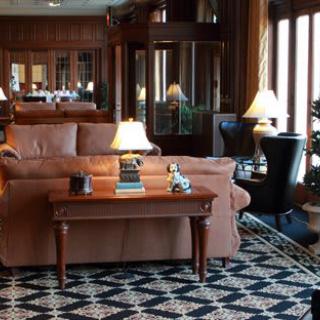 A cozy living room with a leather sofa, a wooden coffee table adorned with books and lamps, and classic wood paneling.