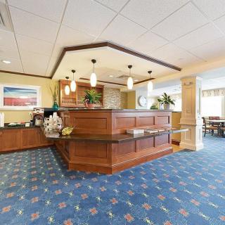 A spacious hotel lobby featuring a wooden reception desk, carpeted flooring, and elegant lighting fixtures.