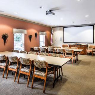 A neatly arranged conference room with tables, chairs, and a projector screen.