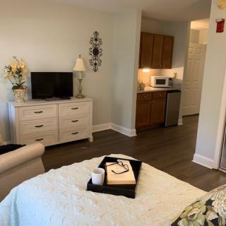 A cozy bedroom with a TV on a dresser, adjacent to a small kitchenette.