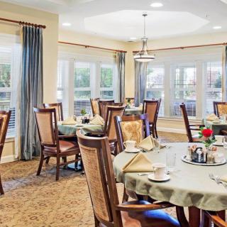 A well-lit dining room with neatly arranged tables and chairs, featuring large windows and elegant decor.