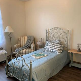 A cozy bedroom with a single metal framed bed, striped armchair, and soft lighting.