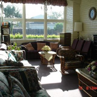 A cozy living room with ample sunlight streaming through large windows, featuring comfortable furniture and a central coffee table.