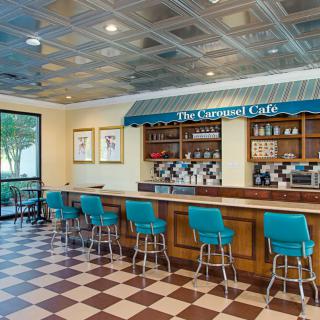 Retro-style cafe interior with a checkered floor and blue barstools at the counter.