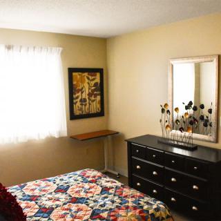 A cozy bedroom with a floral bedspread, dresser, and wall decor.