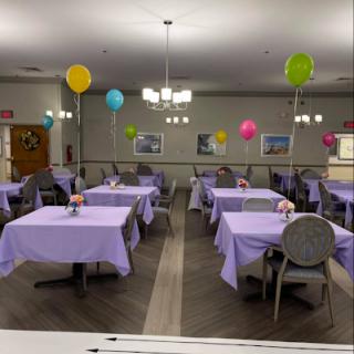 A beautifully decorated dining area ready for a celebration, featuring purple tablecloths and colorful balloons.