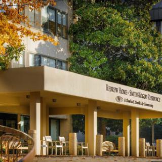 A modern building featuring an inviting entrance and outdoor seating, surrounded by vibrant autumn trees.