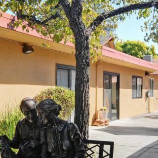 A sculpture of two people sitting on a bench under a tree outside a building.
