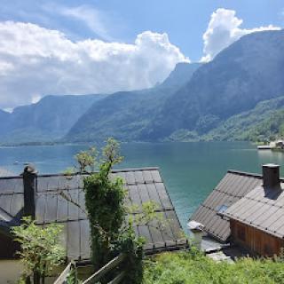 A tranquil lakeside view surrounded by majestic mountains and charming houses under a bright sky.