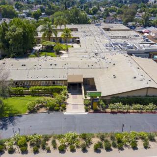 Aerial view of a large building complex with landscaped gardens and a parking lot in a suburban area.
