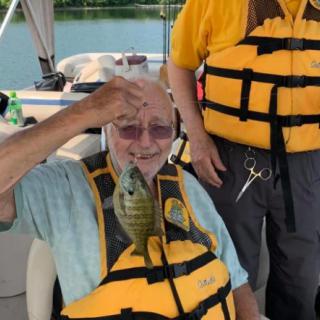 A person on a boat proudly holding up a fish they caught, while wearing a life jacket.