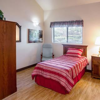 A cozy bedroom with a single bed featuring striped bedding, a wooden dresser, and a nightstand with a lamp beside it.