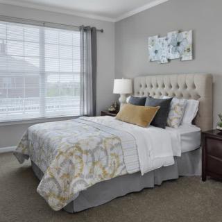 A cozy and well-decorated bedroom with a large bed, bedside table, and natural light from a window.