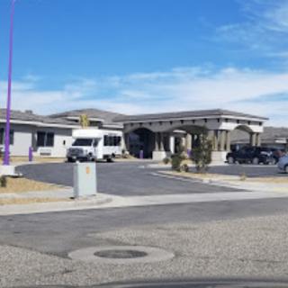 A view of a modern building with a parking lot and several vehicles under a partly cloudy sky.