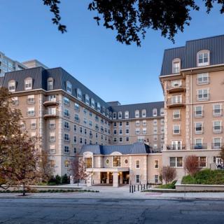 A grand hotel with classic architecture and multiple balconies, surrounded by trees.