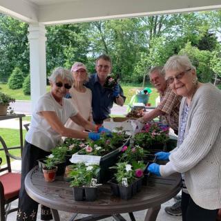 A group of older adults enjoying gardening together outdoors at a table.